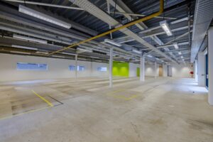 Leeg bedrijfsruimte aan de Laarderhoogtweg met betonnen vloer, zichtbare plafonds en een felgroene accentmuur.