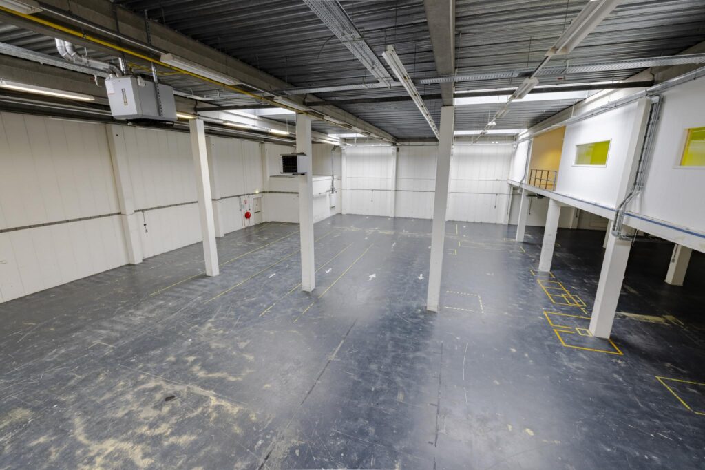 Leeg industrieel magazijn aan de Laarderhoogtweg met betonnen vloer, witte wanden, en entresol met kantoren.