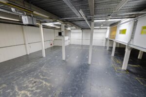 Leeg industrieel magazijn aan de Laarderhoogtweg met betonnen vloer, witte wanden, en entresol met kantoren.