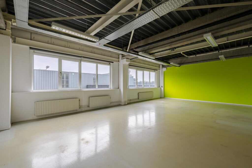 Leeg kantoorruimte aan de Laarderhoogtweg met witte vloer, groen geverfde wand en grote ramen.