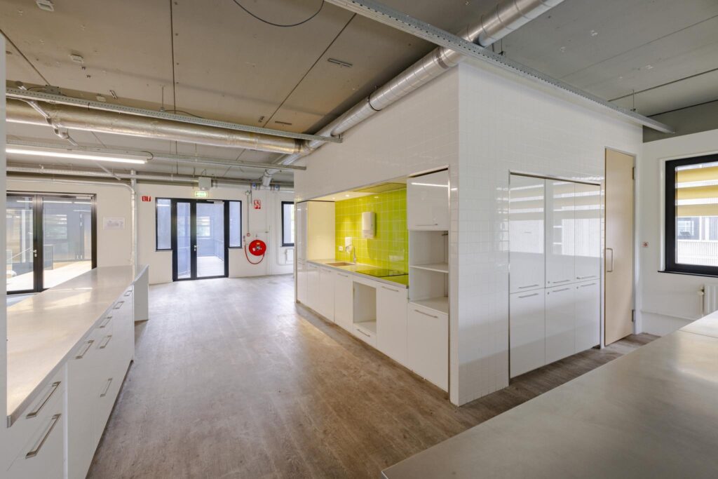 Moderne, open kitchenette met felgroene tegelwand in een licht industrieel kantoorpand aan de Laarderhoogtweg.