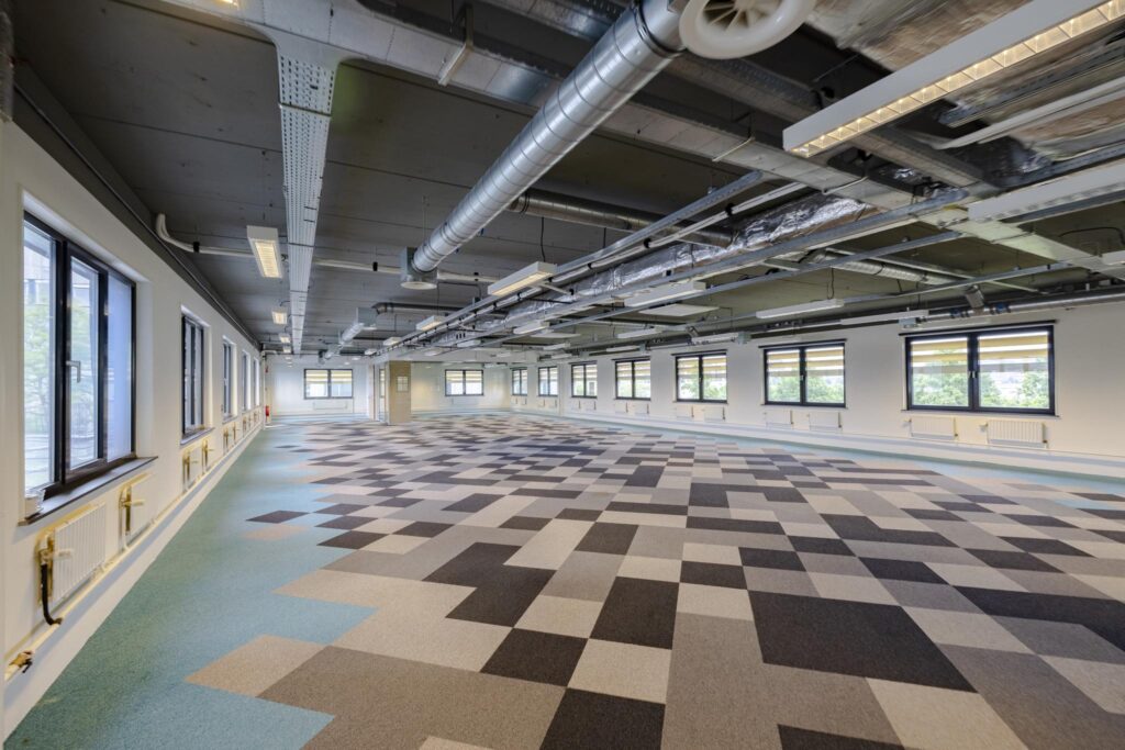 Ruime, lege kantoorruimte aan de Laarderhoogtweg met een modern industrieel plafond en kleurrijke tapijttegels.