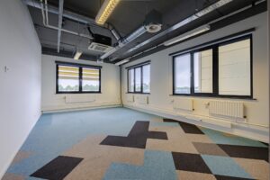 Leeg kantoorruimte aan de Laarderhoogtweg met industrieel plafond en kleurrijke vloerbedekking.