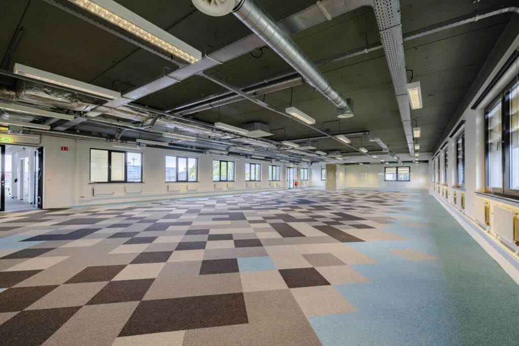 Leeg kantoorruimte aan de Laarderhoogtweg met industriële plafondafwerking en vloerbedekking in patroon van grijze en blauwe vlakken.