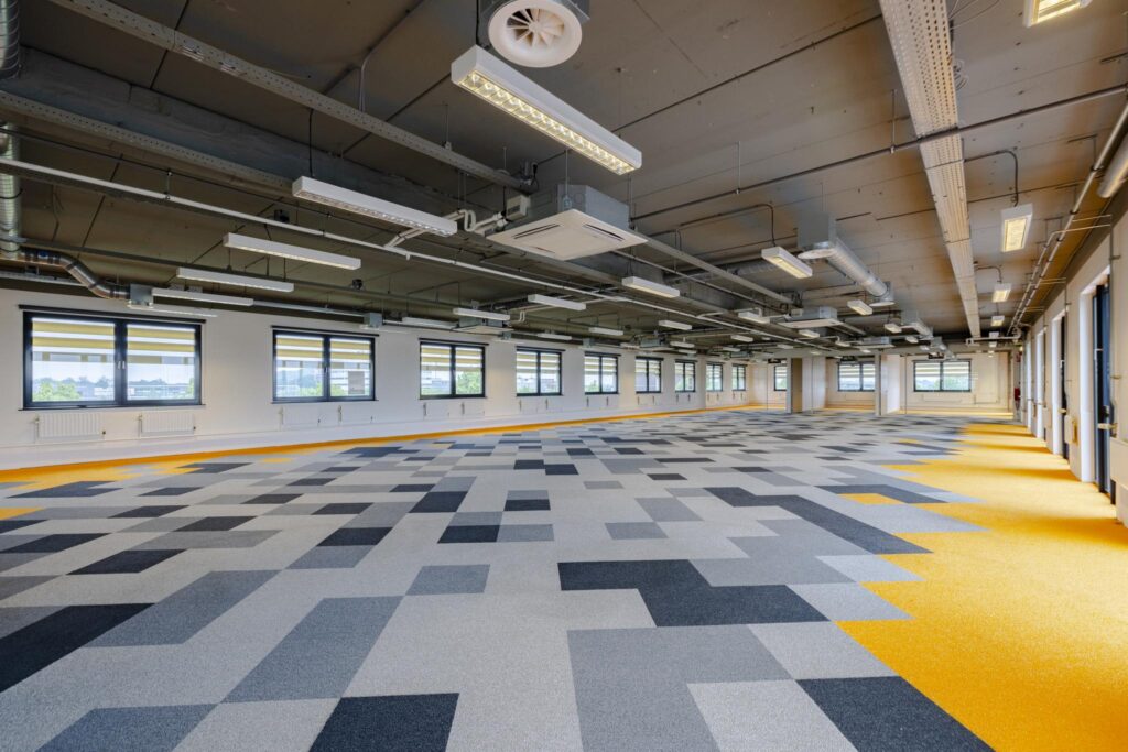 Leeg, modern kantoorinterieur aan de Laarderhoogtweg met een kleurrijke, geometrische vloerbedekking en industriële plafonafwerking.