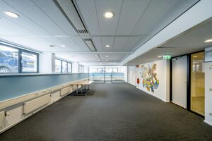 Ruime, lichte kantoorruimte met muurillustratie, glazen wanden en meerdere ramen aan de linkerkant.