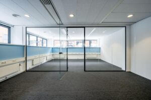 Lichte, lege kantoorruimte met glazen tussenwand en blauw-witte muren aan de Stroombaan.