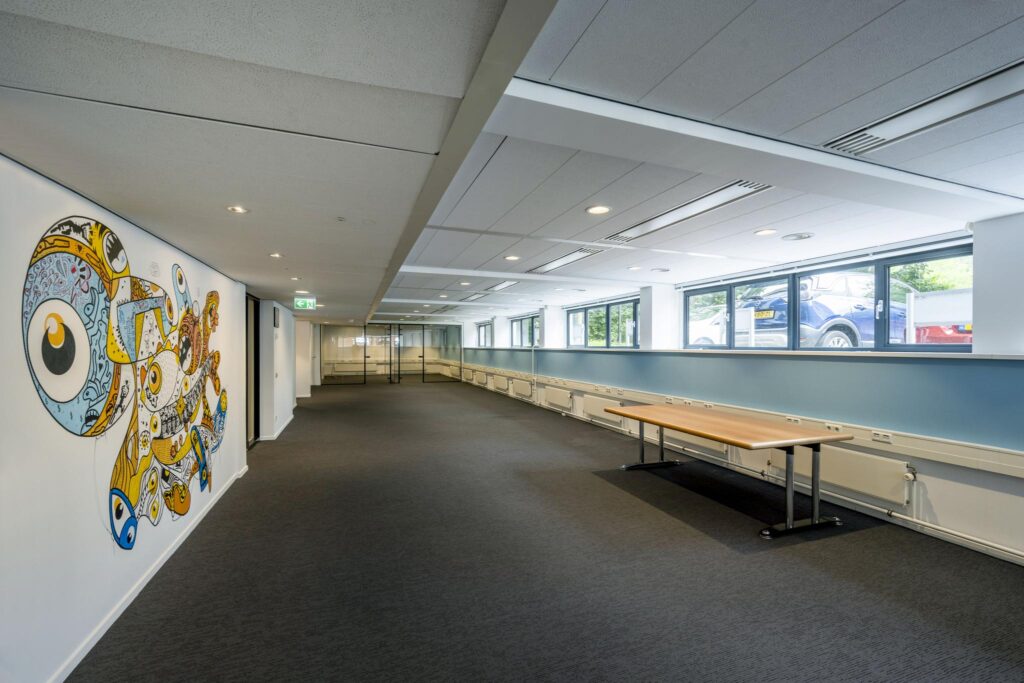 Moderne kantoorruimte met glazen wanden, wandkunst in felle kleuren en een houten tafel langs het raam.