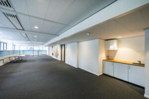Lichte kantoorruimte met een pantry, glazen wand en muurkunst bij de ingang.