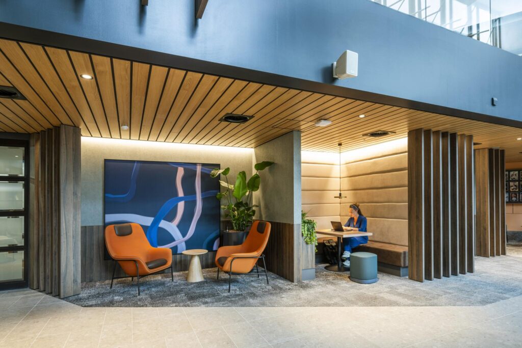 Modern office lounge area at Jachthavenweg with seating, artwork, and a person working on a laptop in a padded booth.
