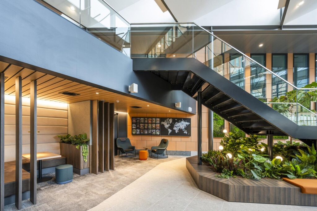 Modern office lobby on Jachthavenweg with indoor greenery, a black staircase, and cozy seating areas.