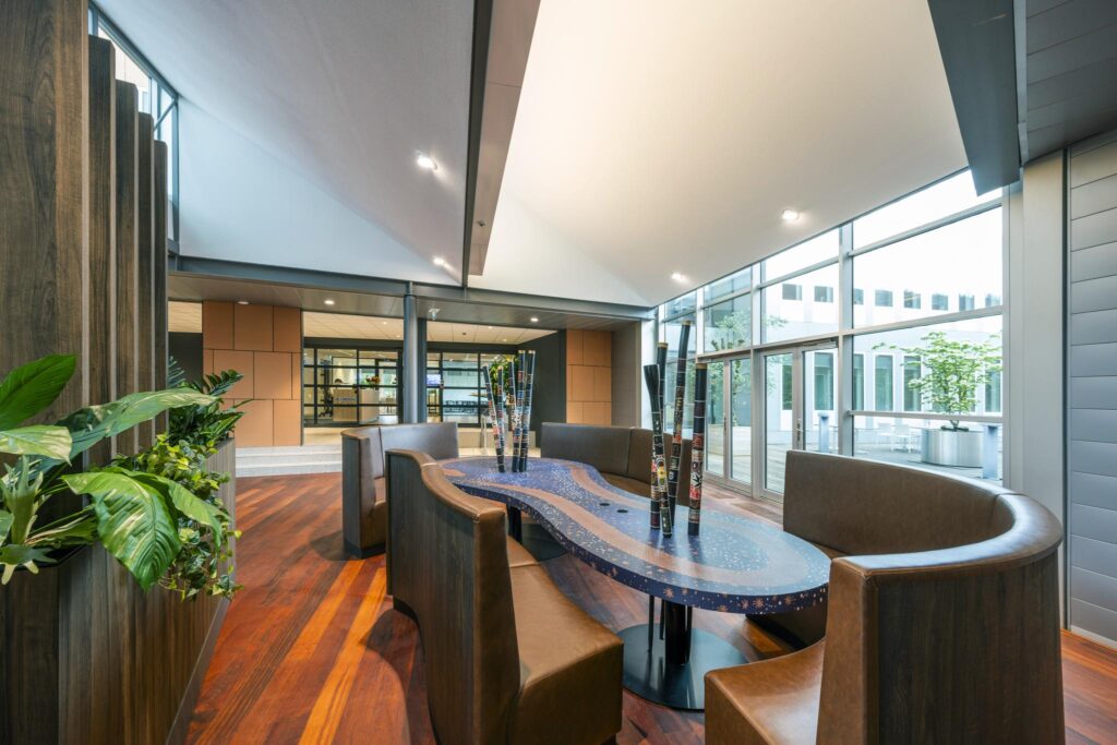 Modern seating area with a custom wavy table and decorative poles in a bright, glass-walled office lobby on Jachthavenweg.