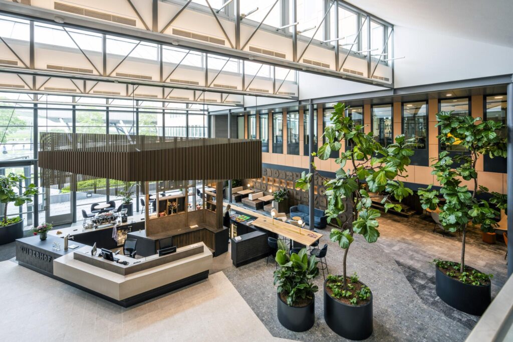 Modern lobby area of the Jachthavenweg office building with a central reception desk, seating areas, and indoor greenery.