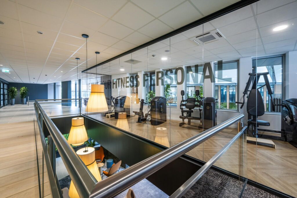 Modern gym area with workout machines behind a glass wall in a sleek office building on Jachthavenweg.