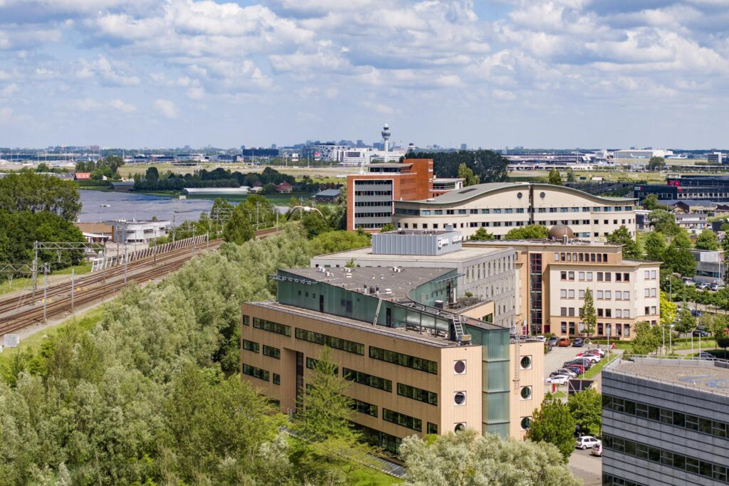 Aerial view of office buildings along Wegalaan in Hoofddorp, with railway tracks and Schiphol Airport visible in the background.