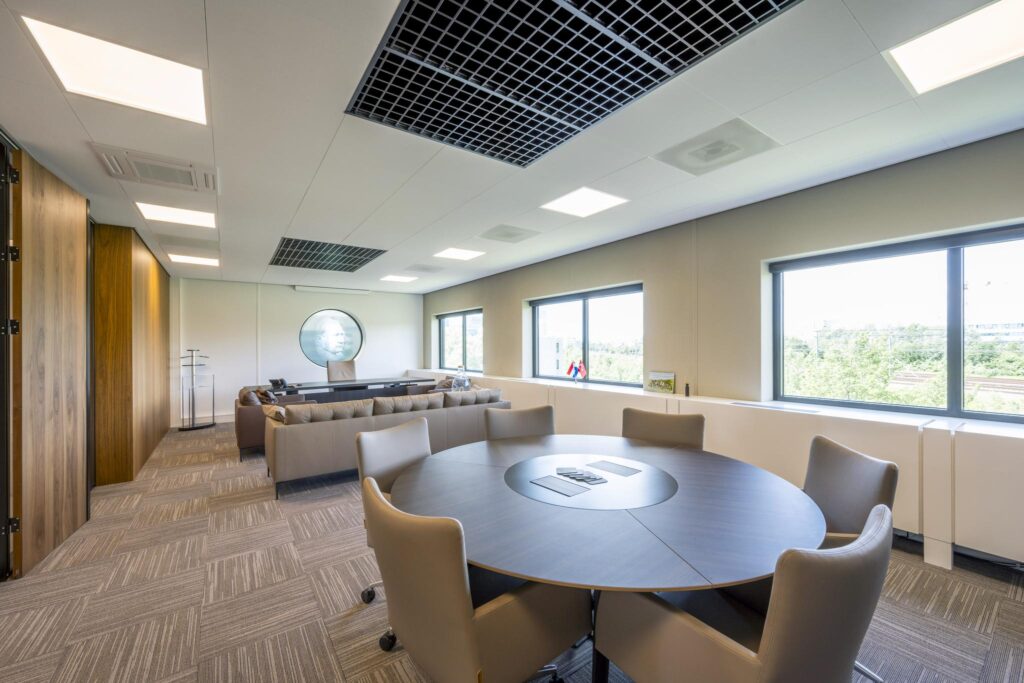 Modern executive office with a round meeting table, large desk, and windows overlooking greenery.