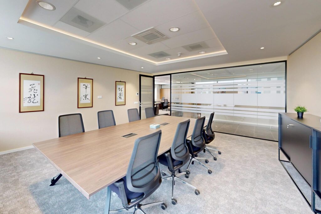 Modern conference room with a large wooden table, office chairs, and framed calligraphy art on the wall.