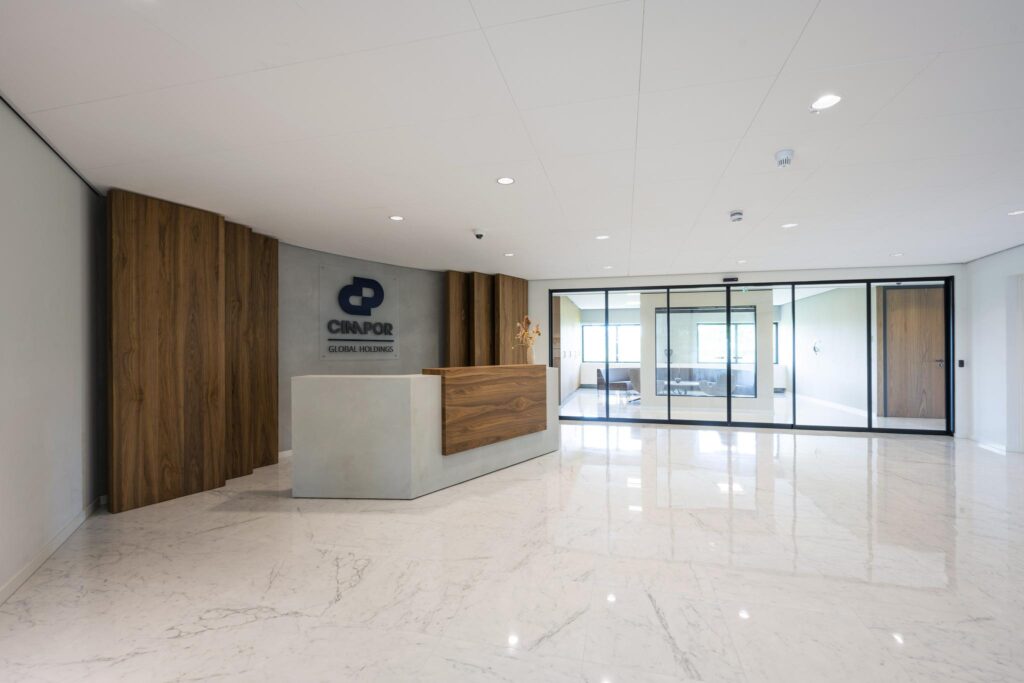 Modern reception area of Cimpor Global Holdings with a wood-accented desk and glass-walled meeting rooms.