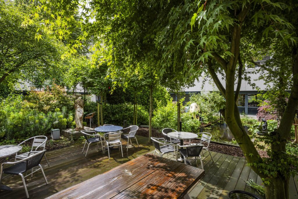 Shaded garden terrace at Diemermeer with outdoor seating, lush greenery, and decorative statues.