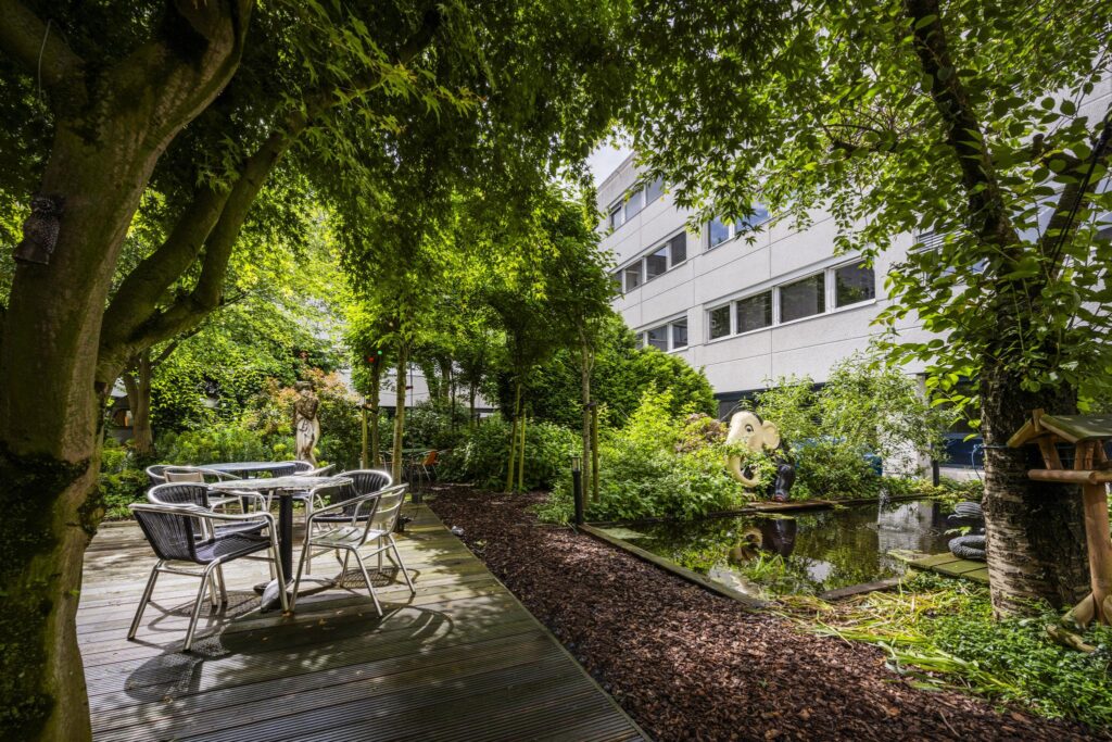 Lush green courtyard garden at Diemermere with seating area, pond, and decorative sculptures.