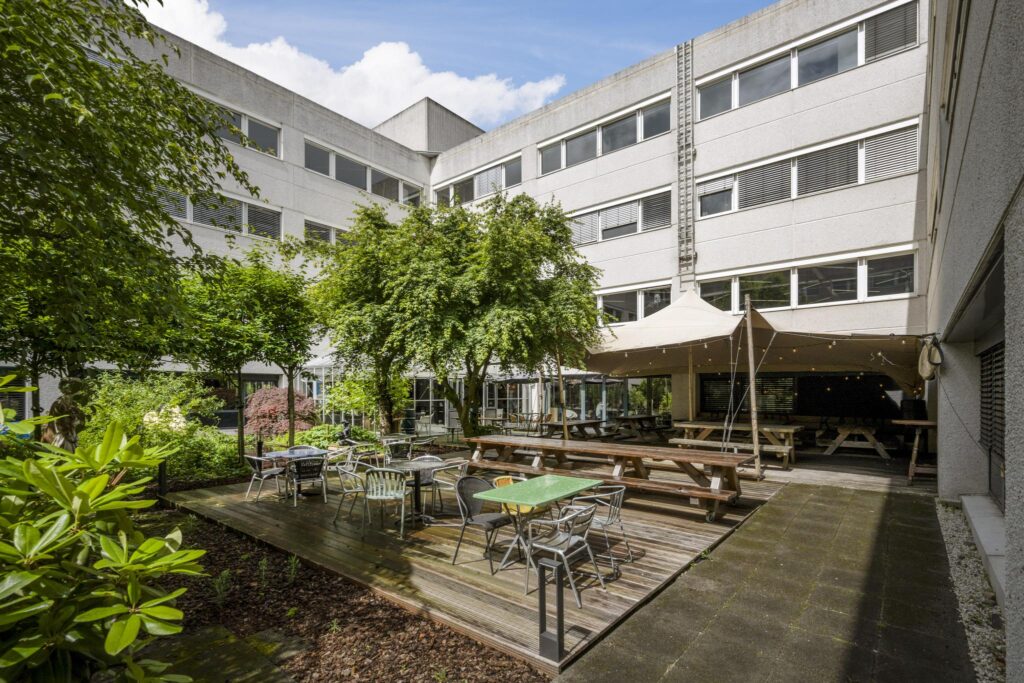 Outdoor courtyard of Diemermeer with seating areas, picnic tables, trees, and a canopy-covered terrace.