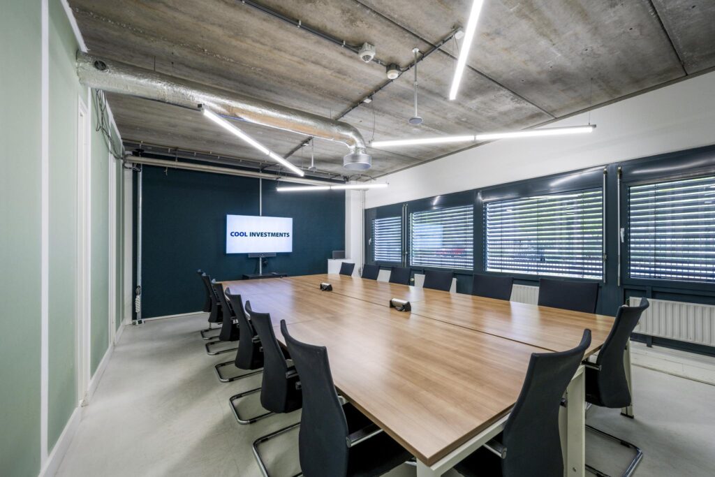 Modern conference room at Diemermere with a long wooden table, black chairs, and a screen displaying "COOL INVESTMENTS".