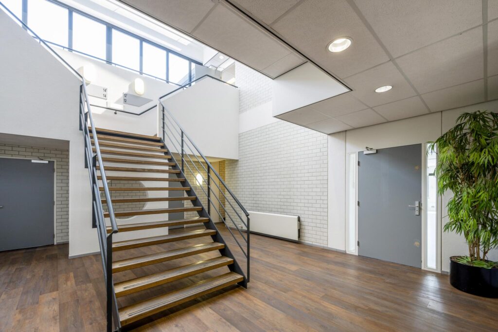 Moderne lichte entreeruimte met houten trap, houten vloer en grijze deuren aan de Breguetlaan.