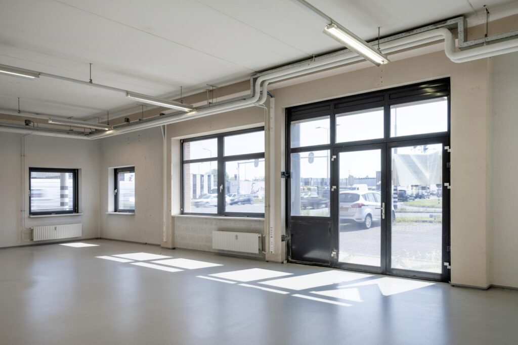 Lichte, lege bedrijfsruimte aan de Breguetlaan met grote ramen en zicht op parkeerterrein.