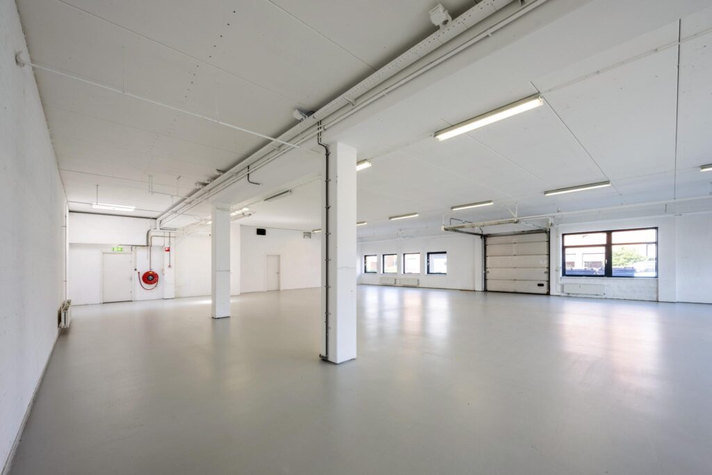 Lichte, lege bedrijfsruimte aan de Breguetlaan met betonnen vloer, grote ramen en overheaddeur.