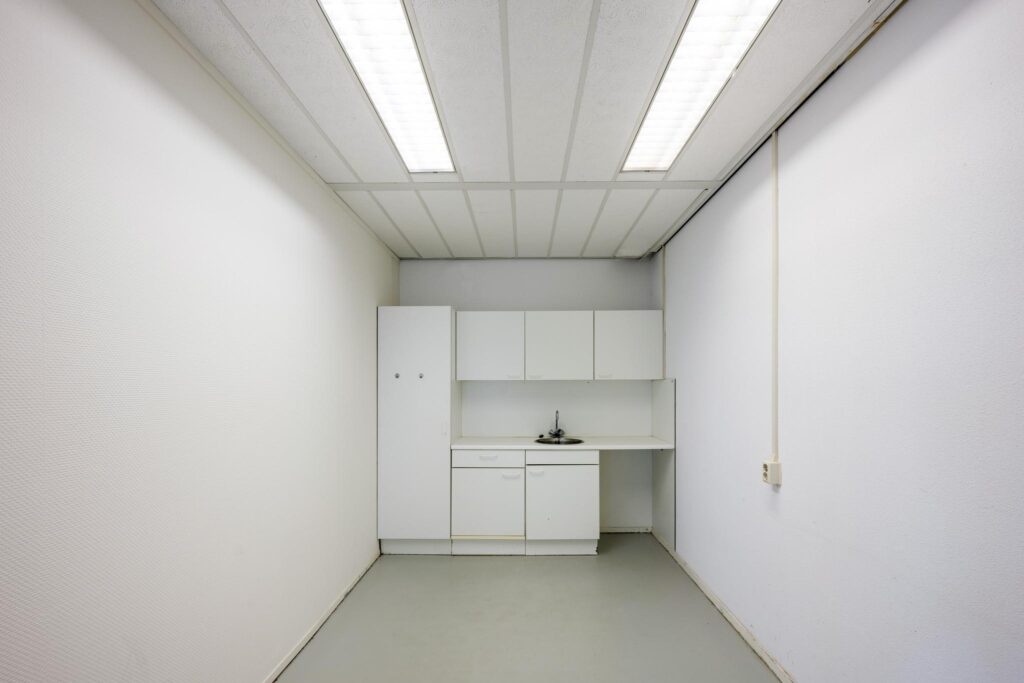 Kleine pantry met witte keukenkastjes en een wasbak in een smalle, witte ruimte aan de Breguetlaan.