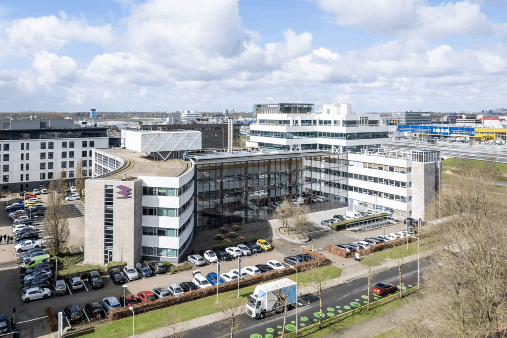 Luchtfoto van een modern kantoorgebouw aan de Paalbergweg in Amsterdam-Zuidoost met parkeerplaatsen en bedrijventerrein op de achtergrond.