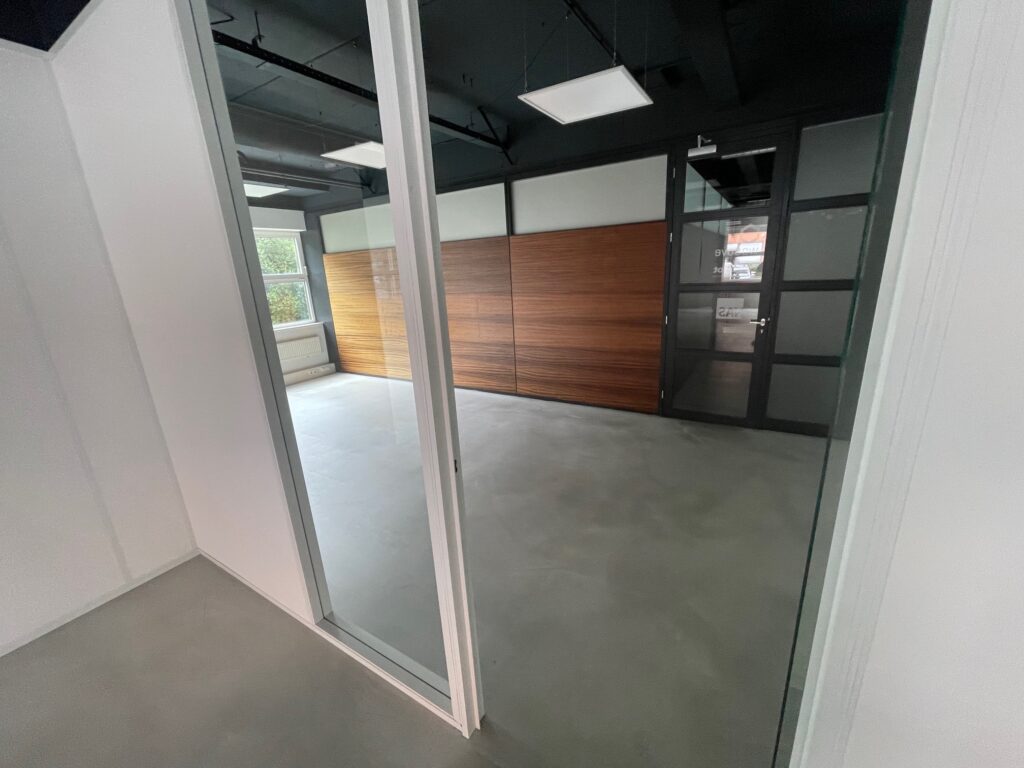 Modern empty office space with glass walls, concrete floor, and wooden panel accents.