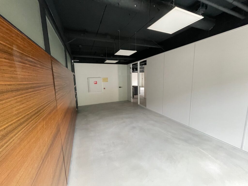 Empty modern hallway with white walls, a wooden panel on the left, and ceiling lights in an office building.