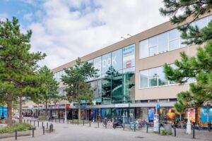 Vooraanzicht van het stadsgebouw 'LINSdok' aan de Helmholtzstraat met winkels, kantoren en geparkeerde fietsen.
