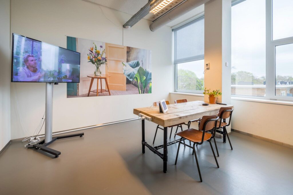Vergaderruimte met houten tafel, stoelen, muurdecoratie, een groot scherm en veel daglicht aan de Helmholtzstraat.