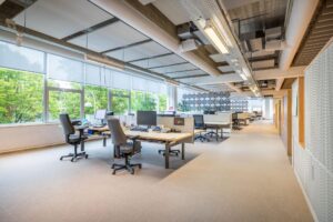 Modern, licht kantoorinterieur aan de Helmholtzstraat met bureaus, bureaustoelen en grote ramen met uitzicht op groen.