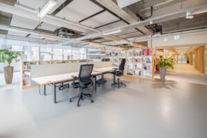 Moderne, lichte kantoorruimte aan de Helmholtzstraat met bureaus, boekenkasten en planten.
