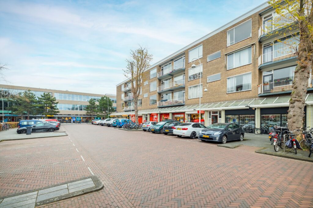 Winkelpand met bovenliggende appartementen aan de Helmholtzstraat met geparkeerde auto's en fietsen op de voorgrond.