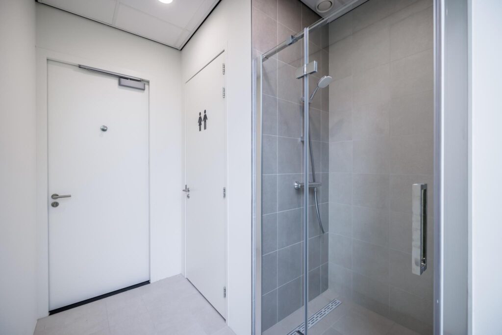 Moderne sanitaire ruimte met een afgesloten douchecabine en twee witte deuren, waarvan één met toiletpictogram.