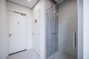Moderne sanitaire ruimte met een afgesloten douchecabine en twee witte deuren, waarvan één met toiletpictogram.