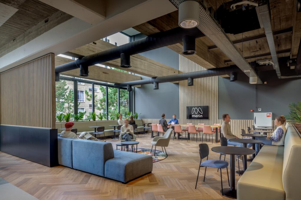 Moderne, open kantoorlounge aan de Helmholtzstraat met zithoeken, vergadertafels en het Merin-logo aan de muur.