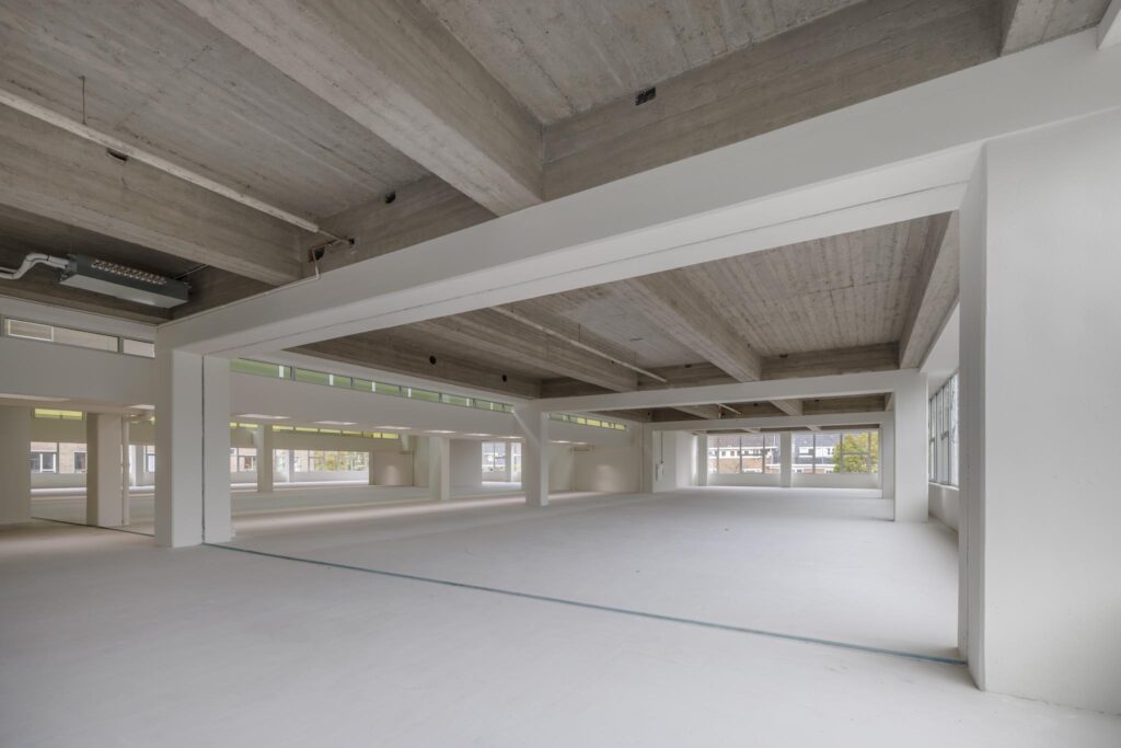 Licht en ruim leeg kantoorpand aan de Helmholtzstraat met betonnen plafond en grote ramen.
