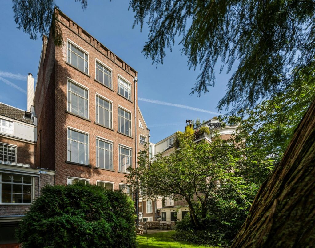 Achterzijde van een karakteristiek herenhuis aan de Herengracht met grote ramen en groene binnentuin.