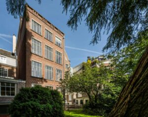 Achterzijde van een karakteristiek herenhuis aan de Herengracht met grote ramen en groene binnentuin.