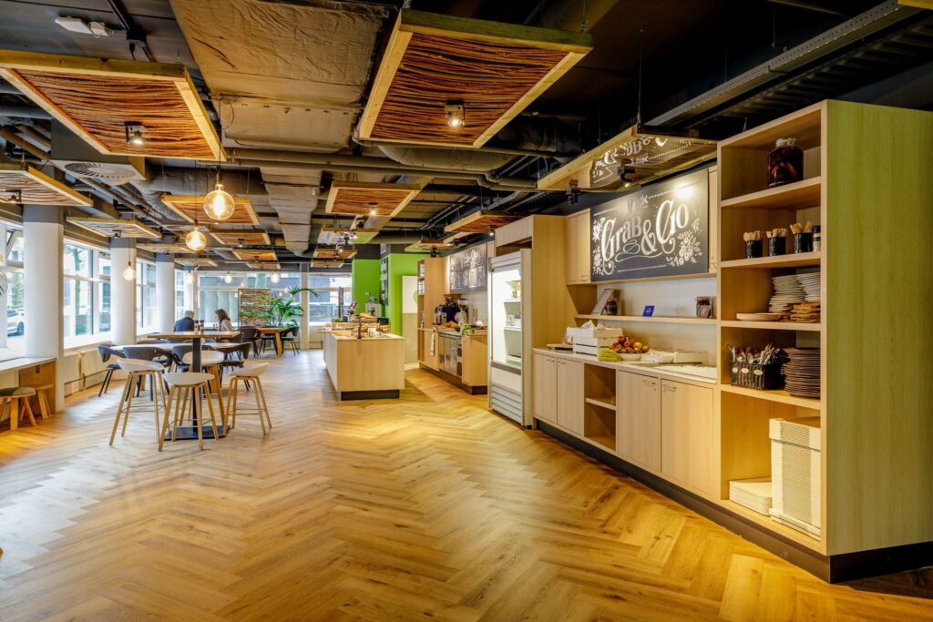 Moderne bedrijfskantine aan de Hullenbergweg met houten vloer, zithoeken en een zelfbedieningsstation genaamd "Grab & Go".