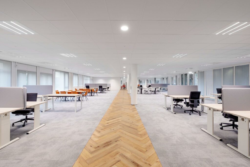 Ruim en modern kantoorinterieur aan de Hullenbergweg met open werkplekken, vergadertafels en een houten looppad.