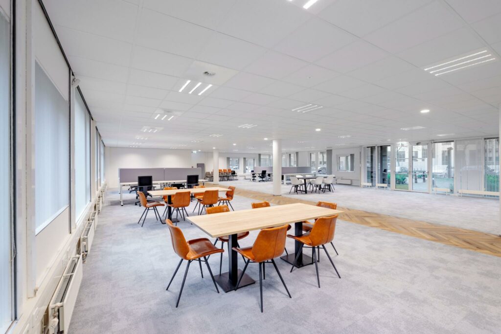 Ruim en modern kantoorinterieur aan de Hullenbergweg met flexibele werkplekken en leren stoelen rond houten tafels.