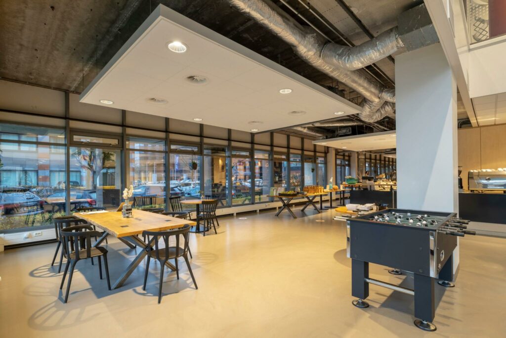 Moderne en ruime kantoorlounge aan de Karspeldreef met grote ramen, zithoeken, een tafelvoetbaltafel en een open keuken.