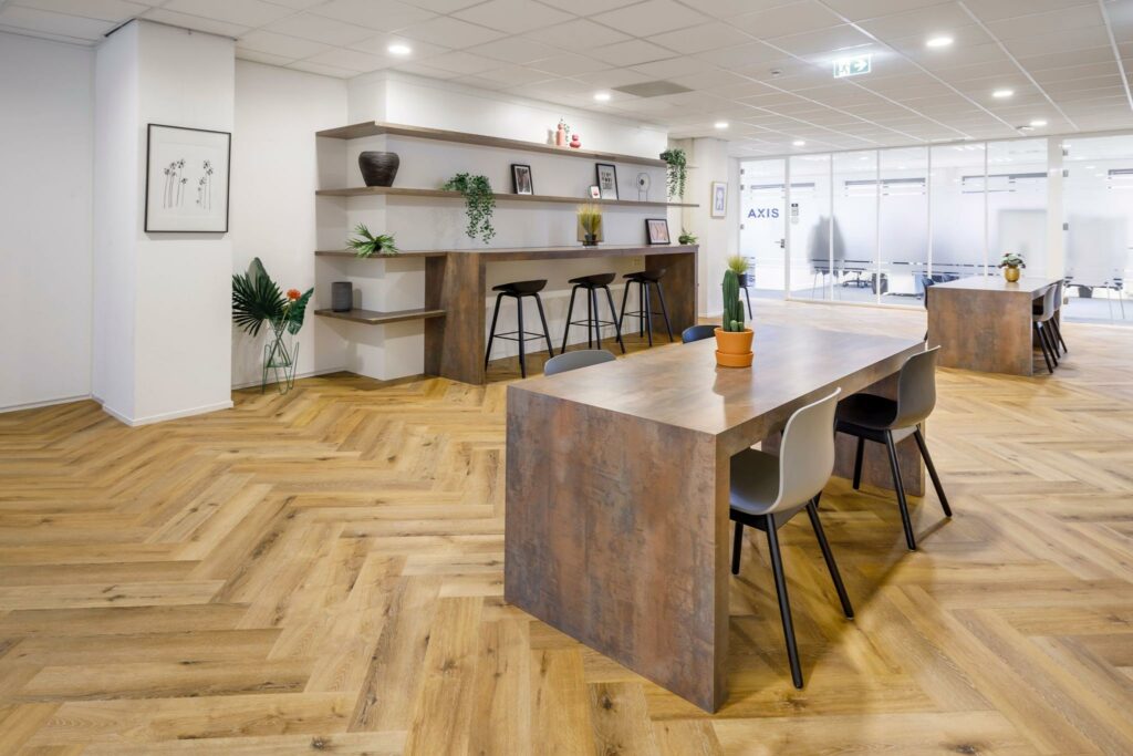 Moderne kantoorruimte aan de Karspeldreef met houten visgraatvloer, grote werktafels en open wandrekken met decoratie.