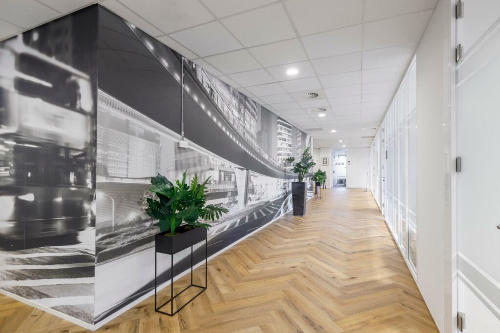 Moderne kantoorhal aan de Karspeldreef met houten visgraatvloer, zwart-wit muurfoto en groene planten.